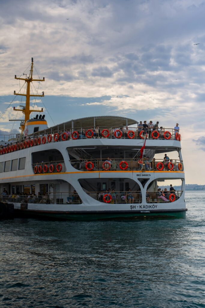 A ferry with passengers on the Bosphorus in Istanbul, Turkey, under a cloudy sky.